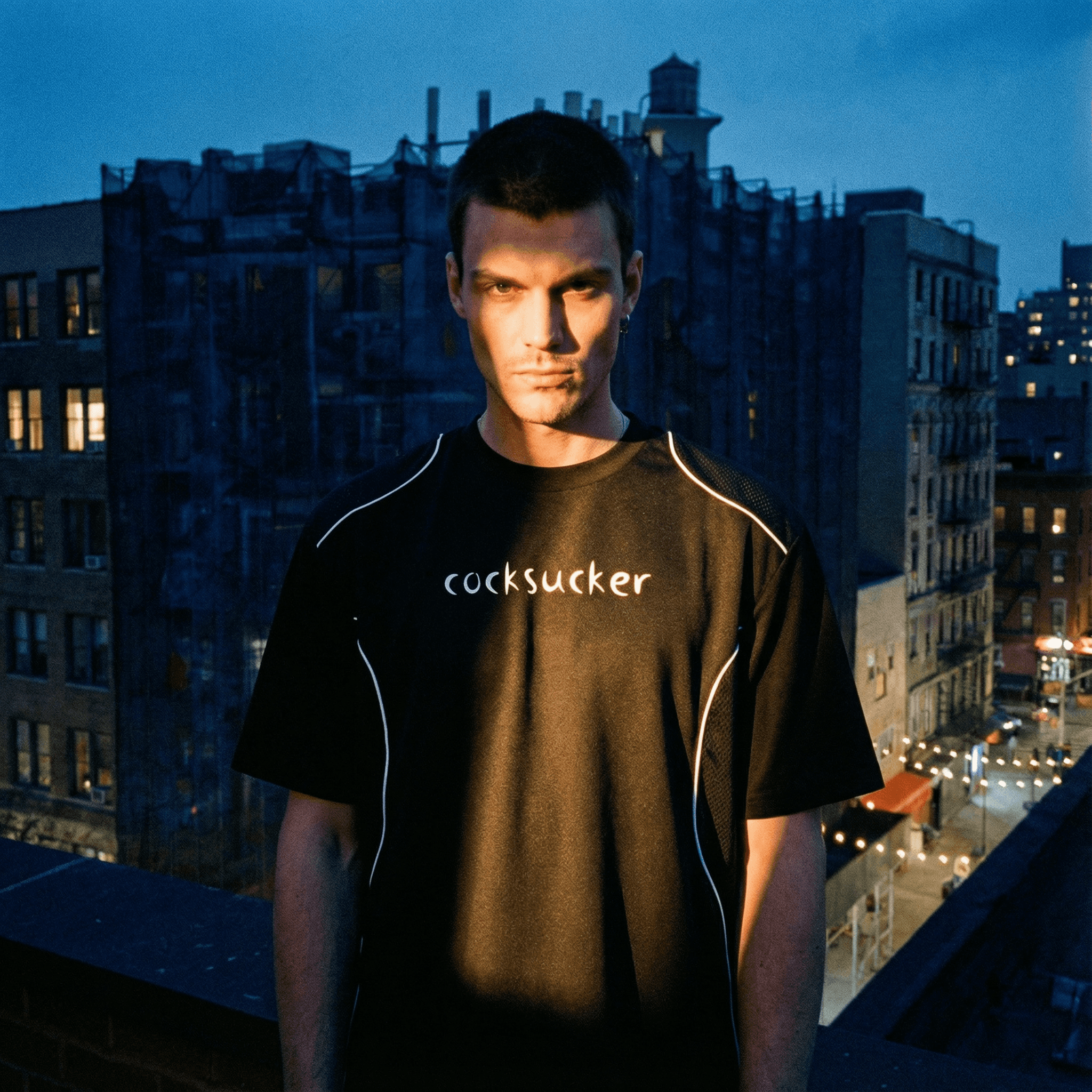 Black contrast piped fetish t-shirt with white piping and bold text worn by male model outdoors at dusk