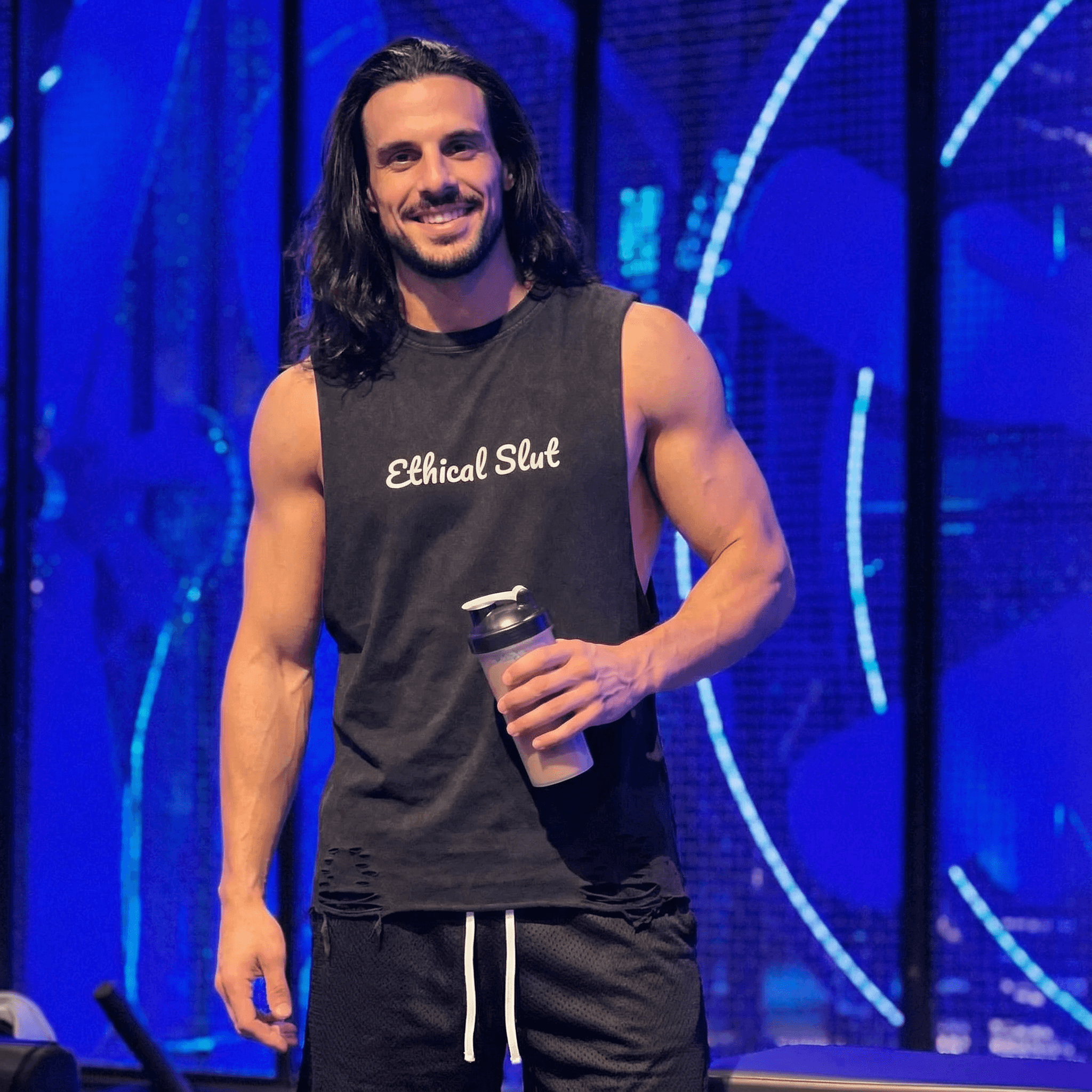 Man wearing black snow washed raw-hem tank top with Ethical Slut text holding a shaker bottle