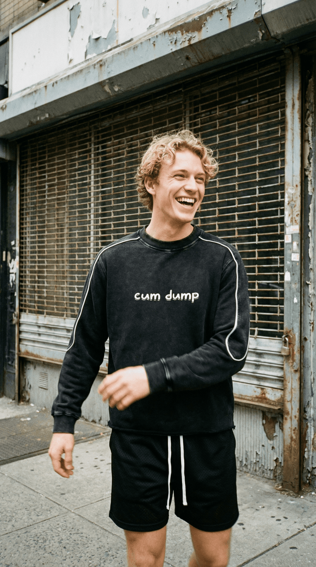 Smiling man wearing black fetish raw hem sweatshirt with white text and matching black shorts outdoors