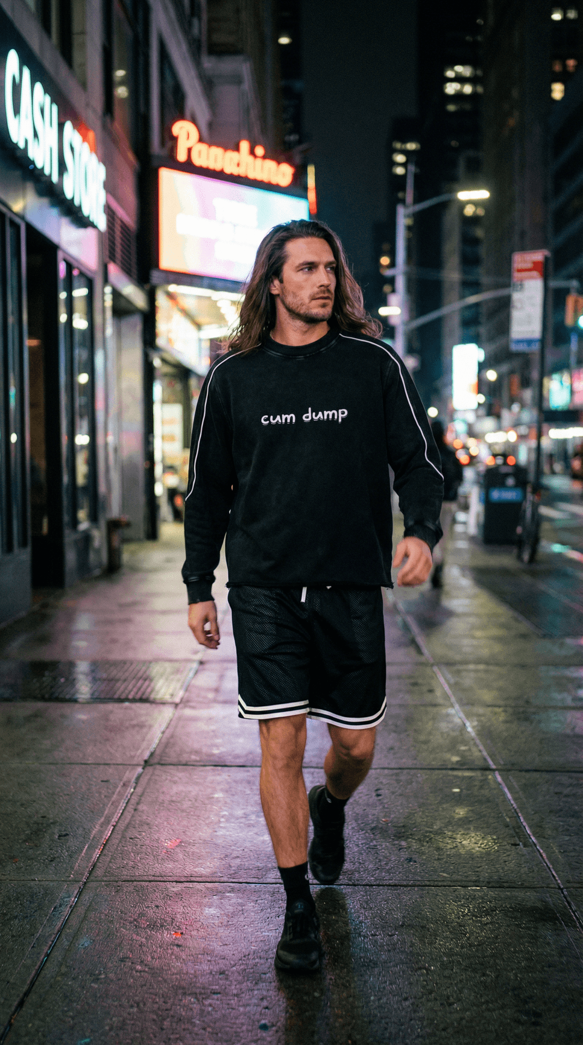 Man walking at night wearing Fetish raw hem sweatshirt with white text and black shorts on city street