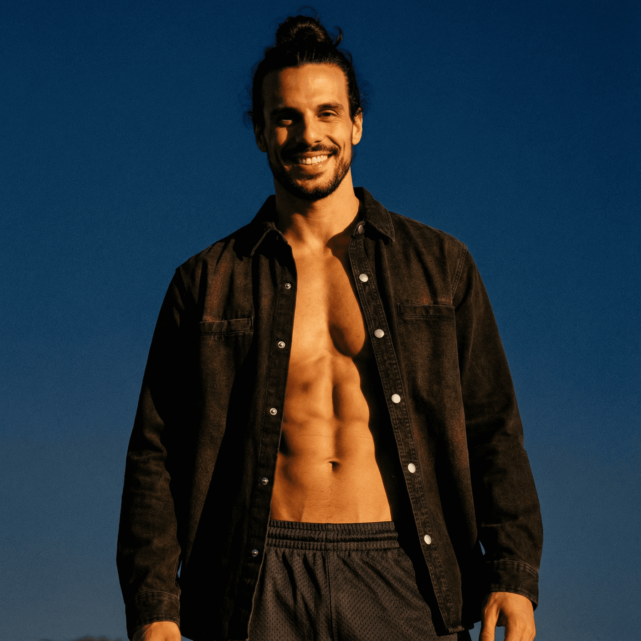 Smiling man wearing a denim vintage washed heavyweight jacket open over bare chest outdoors