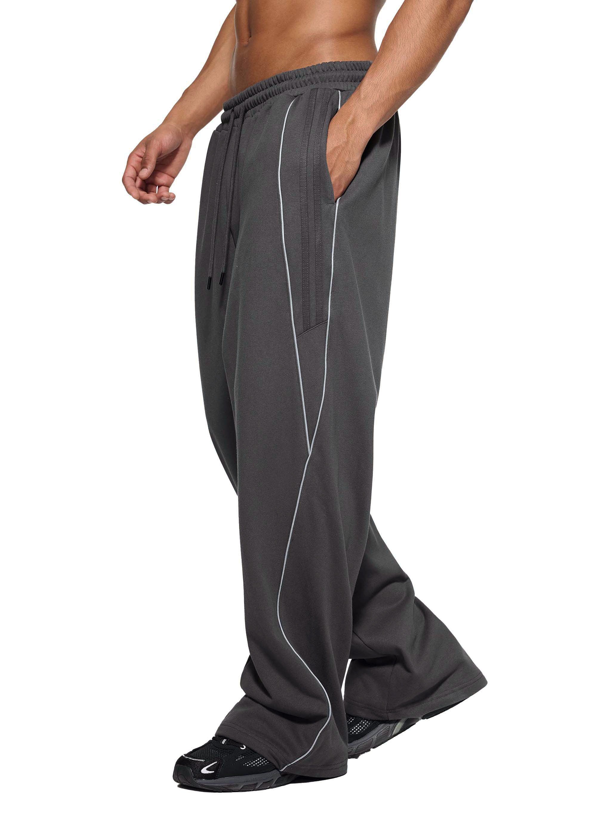 Side view of man wearing FETISHISTO reflection striped sweatpants in dark gray with tapered legs and pockets