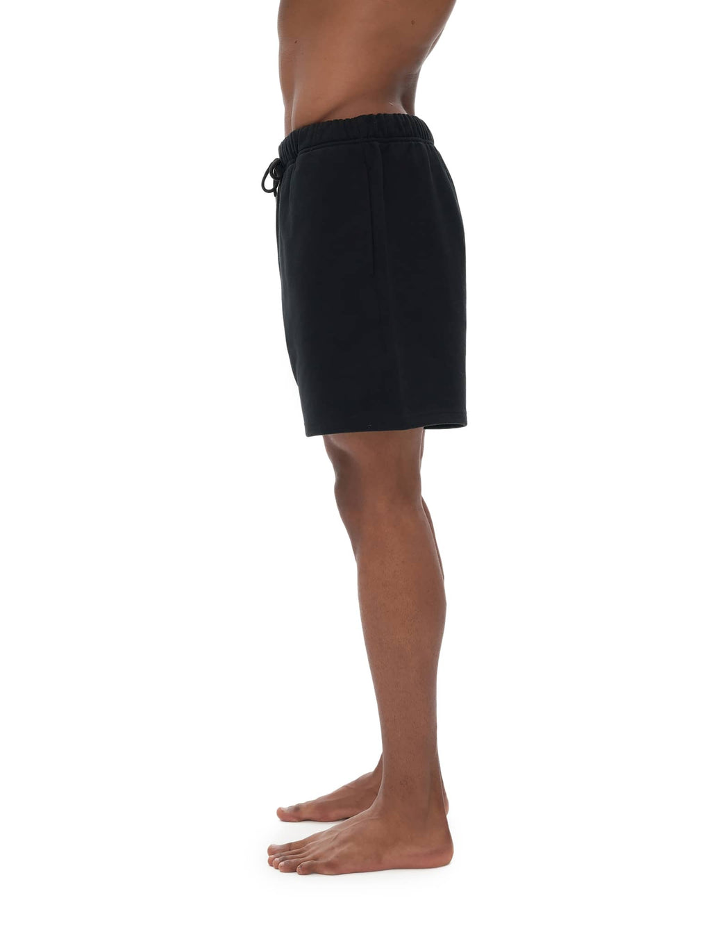Side view of man wearing black FETISHISTO unisex heavyweight fleece shorts with elastic waistband