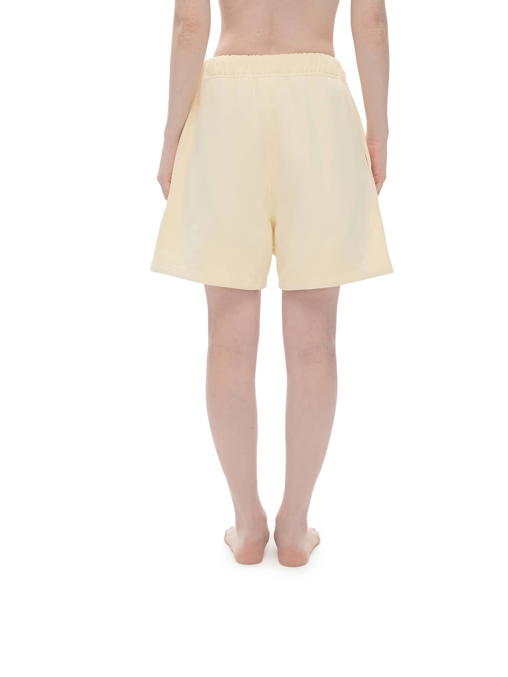 Back view of person wearing beige unisex heavyweight fleece shorts by FETISHISTO with elastic waistband