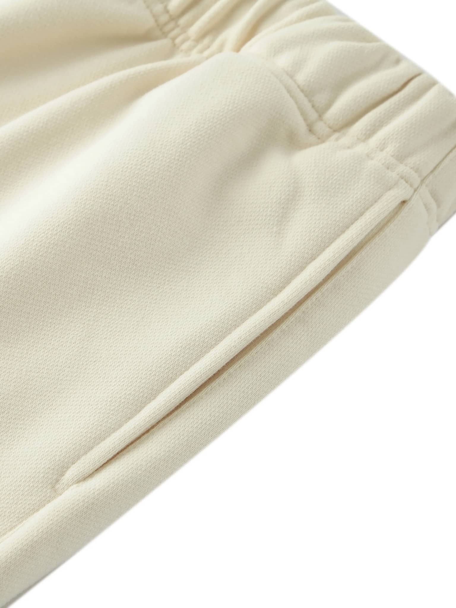 Close-up of cream-colored unisex heavyweight fleece shorts showing elastic waistband and side pocket detail